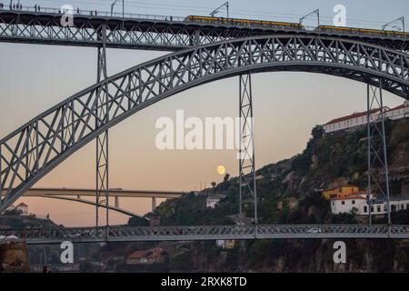 Die berühmte Porto Brücke Ponte Luis am Abend mit Blick von unten. Porto-Brücke in der Dämmerung mit Mond im Hintergrund. Portugiesischer Fluss Douro mit U-Bahn-Brücke. Stockfoto