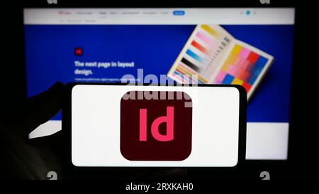 Person, die ein Smartphone mit dem Logo der Desktop-Publishing-Software Adobe InDesign auf dem Bildschirm vor der Website hält. Konzentrieren Sie sich auf das Display des Telefons. Stockfoto
