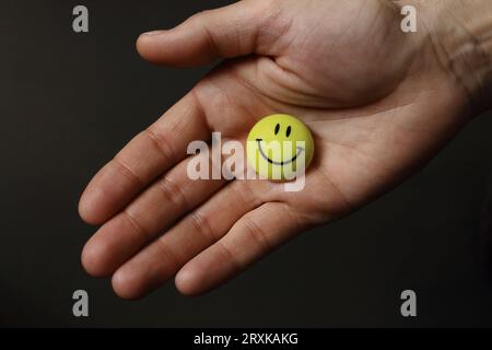 Gelbes lächelndes Gesicht auf offener Handfläche. Rundes Lächeln mit offener Hand. Konzept des Friendship Day. Fröhliche Emotionen. Freundschaftsvorschlag. Stockfoto