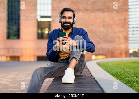 Arabischer Mann mit Mobiltelefon und Kopfhörern im urbanen Raum Stockfoto