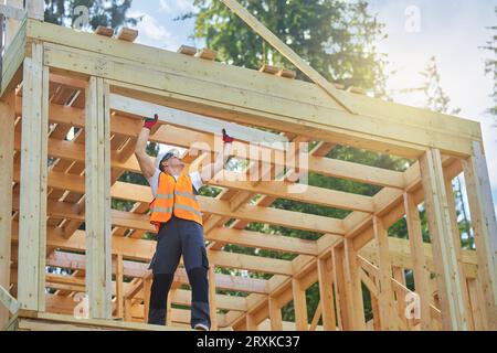 Baumeister trägt Uniforn, Weste und Helm, hält, hebt Holz gilder, Brett. Stockfoto