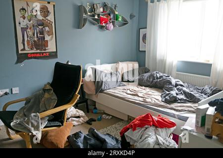 Unordentliches Schlafzimmer mit Teenager-Jungen und ungebastelten Bettwäsche Gorillaz-Posterstuhl grau-blaue Wände Wandfarbe bemalt Großbritannien Großbritannien 2023 KATHY DEWITT Stockfoto