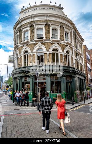 Ein Mann und eine Frau in einem roten Kleid betreten das Commercial Tavern Pub auf der Commercial Road, Spitalfields, London E1 Stockfoto