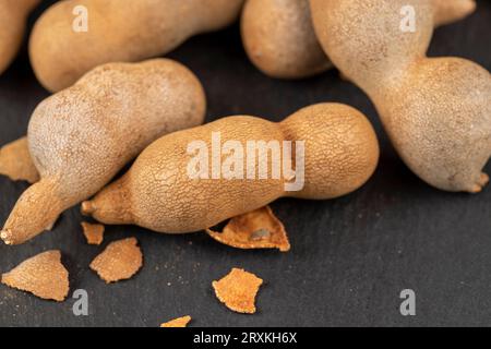 Geschlossene, lange reife Tamarindenschoten aus der Nähe, verzehrfertige ganze Tamarindenfrüchte liegen auf dem Tisch Stockfoto