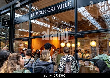 Leute, die Schlange stehen, um in das beliebte Dessertrestaurant Humble Crumble am Old Spitalfileds Market, London E1, zu kommen Stockfoto