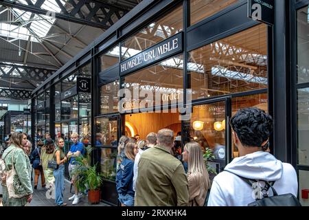 Leute, die Schlange stehen, um in das beliebte Dessertrestaurant Humble Crumble am Old Spitalfileds Market, London E1, zu kommen Stockfoto