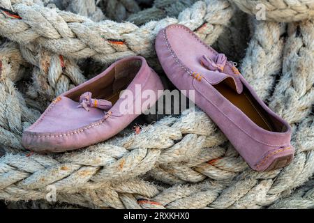 Ein Paar rosafarbene Deckschuhe oder Segelschuhe, die zum Trocknen auf einer Spule eines alten Schiffseils am Hafen liegen Stockfoto