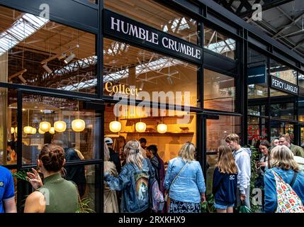 Leute, die Schlange stehen, um in das beliebte Dessertrestaurant Humble Crumble am Old Spitalfileds Market, London E1, zu kommen Stockfoto