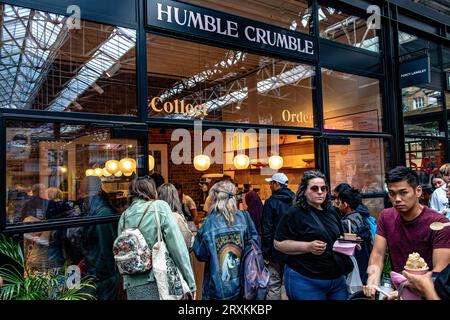 Leute, die Schlange stehen, um in das beliebte Dessertrestaurant Humble Crumble am Old Spitalfileds Market, London E1, zu kommen Stockfoto