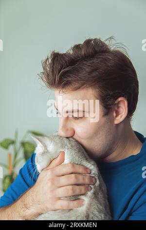 Nahaufnahme des Gesichts eines Mannes, der seine süße schnurrende britische Katze hält. Die Beziehung zwischen Haustieren und Menschen, Liebe, Zuneigung. Stockfoto