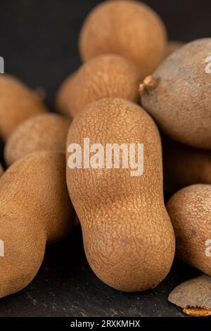 Geschlossene, lange reife Tamarindenschoten aus der Nähe, verzehrfertige ganze Tamarindenfrüchte liegen auf dem Tisch Stockfoto