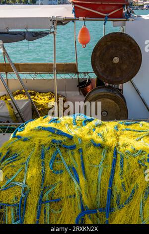 Fischernetze trocknen in der Sonne auf einem alten traditionellen griechischen Fischerboot mit rostigen Winden und Deckausrüstung, die ein nautisches Motiv bilden. Stockfoto