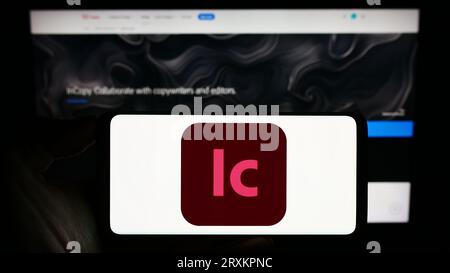 Person, die ein Mobiltelefon mit dem Logo der Textverarbeitungssoftware Adobe InCopy auf dem Bildschirm vor der Geschäftswebseite hält. Konzentrieren Sie sich auf das Display des Telefons. Stockfoto