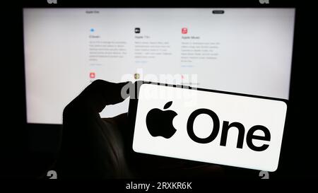 Person, die ein Mobiltelefon mit dem Logo des Abonnementdienstes Apple One auf dem Bildschirm vor der Geschäftswebseite hält. Konzentrieren Sie sich auf das Display des Telefons. Stockfoto