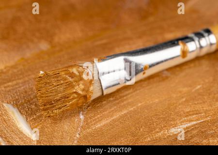 Künstlerische Pinsel beim Malen auf Leinwand mit Goldfarben, mit Goldfarben und Goldschattierungen für kreative Arbeit Stockfoto