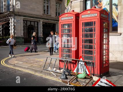 Zwei verblasste und verfallene, aber immer noch funktionierende traditionelle rote Telefonkästen neben den Straßenschildern in Piccadilly im Zentrum von London, Großbritannien. Stockfoto