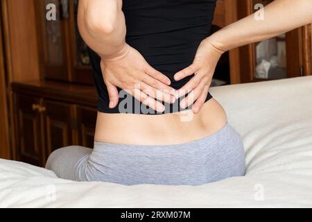 Ein junges Mädchen hält ihren Rücken wegen Rückenschmerzen, sitzt zu Hause auf ihrem Bett, akuten Rückenschmerzen, starken Schmerzen Stockfoto