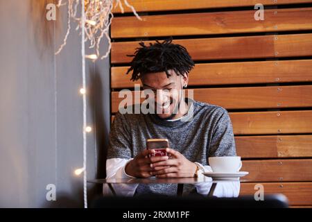 Junger Mann mit Smart Phone im Cafe Stockfoto