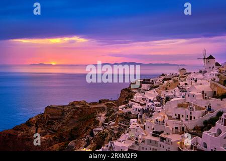 Wunderschöner Blick auf das Dorf Oia mit traditionellen weiß getünchten Häusern und Windmühlen, Insel Santorin, bei Sonnenuntergang, Griechenland. Malerischer Reisehintergrund, berühmtes Reiseziel, farbenfroher Himmel und Wolken. Stockfoto