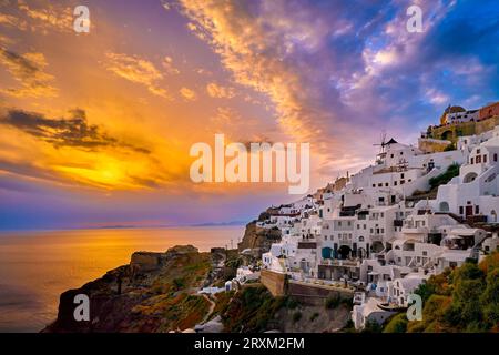 Wunderschöner Blick auf das Dorf Oia mit traditionellen weiß getünchten Häusern und Windmühlen, Insel Santorin, bei Sonnenuntergang, Griechenland. Malerischer Reisehintergrund, berühmtes Reiseziel, farbenfroher Himmel und Wolken. Stockfoto