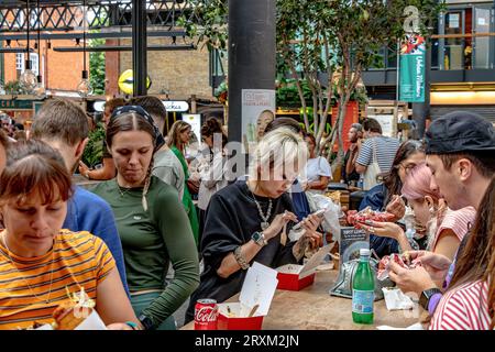 Leute, die Essen von verschiedenen Lebensmittelverkäufern in der Lebensmittelhalle im Old Spitalfields Market, London E1, genießen Stockfoto