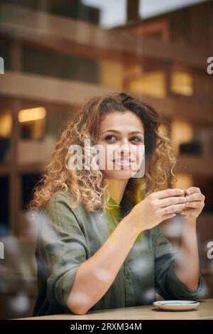 Junge Frau mit Tasse Kaffee hinter Fenster Cafe Stockfoto