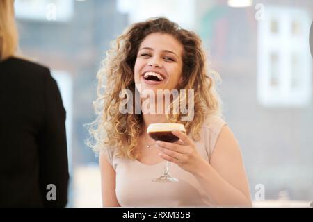 Lachende junge Frau mit Espresso Martini Stockfoto