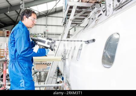 Mann, der im Hangar ein Elektrowerkzeug im Flugzeug benutzt Stockfoto