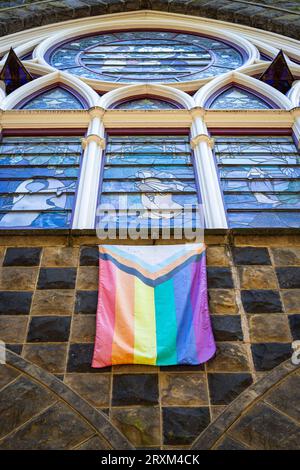 Die Flagge des Pride hängt unter einem Buntglasfenster an der Vorderseite einer Kirche im Zentrum von Portland, Oregon Stockfoto