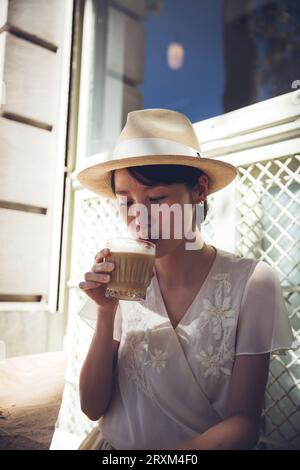Junge Frau mit Strohhut, die Eiskaffee trinkt Stockfoto