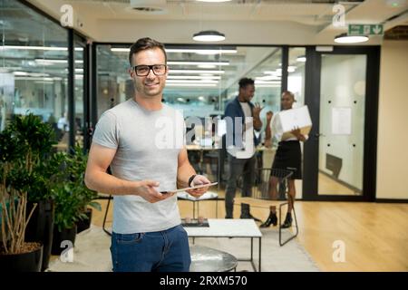 Lächelnde junge Unternehmer holding Tablette im Büro Stockfoto