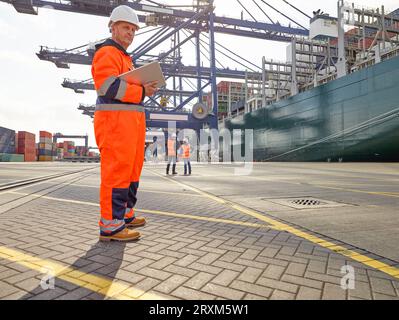 Hafenarbeiter mit digitalen Tablet neben Frachter im Hafen von Felixstowe, England Stockfoto