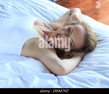 Junge Frau, die auf weißen Bett liegend Stockfoto