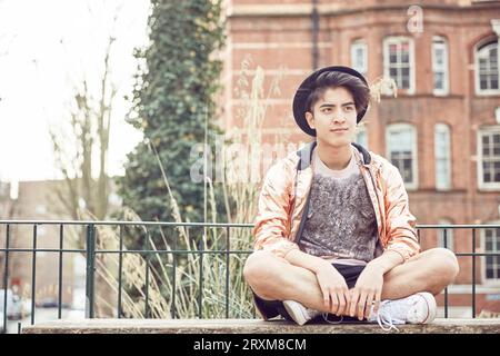 Teenager Junge sitzt im Schneidersitz auf der Parkbank Stockfoto