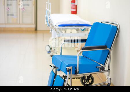Spezieller blauer gepolsterter Rollstuhl mit Krankenhaustrage im Korridorhintergrund Stockfoto