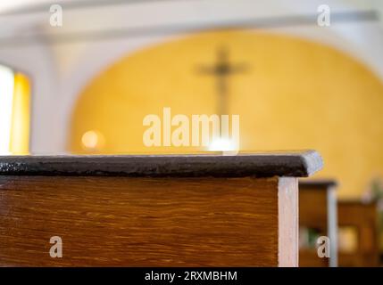 Dunkelbraune Kirchenbänke mit hellgelbem Hintergrund aus Altar und Kruzifix Stockfoto