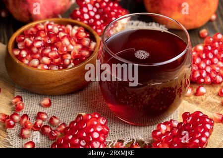 Süßer und saurer Granatapfelsaft in einem transparenten Glas auf dem Tisch, daneben rote reife Granatäpfel mit großen süßen Körnern Stockfoto