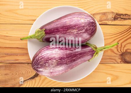 Zwei reife Auberginen mit weißer Keramikplatte auf Holztisch, Makro, Draufsicht. Stockfoto