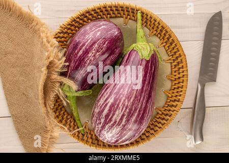 Zwei reife Auberginen mit Keramikplatte und Messer auf Holztisch, Makro, Draufsicht. Stockfoto