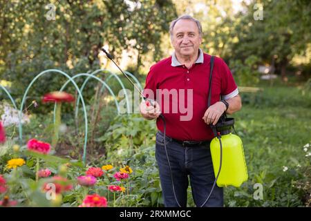 Reifer Mann, der beim Lächeln auf Blumen im Garten Insektizid aufträgt Stockfoto