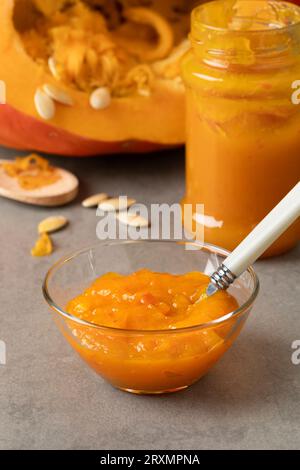 Glasschale mit hausgemachter oranger Kürbismarmelade aus nächster Nähe vor einem frischen Kürbis Stockfoto