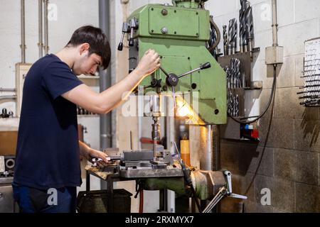 Professioneller Arbeiter, der in einer Metallwerkstatt ein Stahlstück mit einer Industriemaschine bohrt. Mechanische Maschinen. Stockfoto