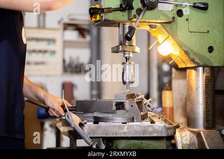 Professioneller Arbeiter, der in einer Metallwerkstatt ein Stahlstück mit einer Industriemaschine bohrt. Mechanische Maschinen. Stockfoto