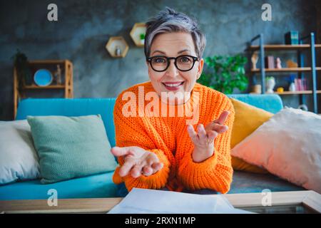 Foto von bezauberndem glücklichen Reifen Dame gekleideten orangefarbenen Pullover, der Videogespräche im Haus führt Stockfoto