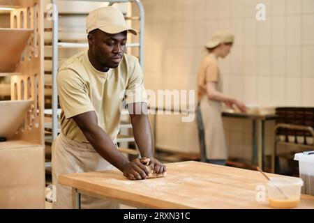 Porträt des jungen Schwarzen Mannes, der Teig knabbert, während er in einer handwerklichen Bäckerei arbeitet, Kopierraum Stockfoto