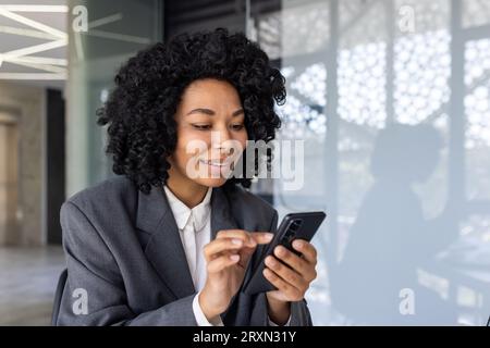 Erfolgreiche Geschäftsfrau nutzt Smartphone im Büro aus nächster Nähe, lächelnder Mitarbeiter nutzt App am Telefon, gibt Nachrichten ein und durchsucht Internetseiten online. Stockfoto