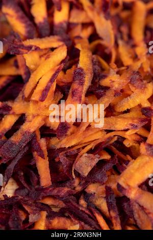 In der Küche in dünne Scheiben von rot-orangefarbenen Karotten geschnitten, mehrere von Schmutz gereinigt und gewaschene Karotten in Stücke geraspelt auf einer Reibe Stockfoto