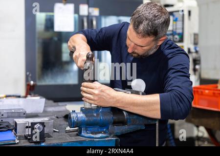 Professioneller Arbeiter, der in einer Metallwerkstatt an einem Stahlstück mit Hammer arbeitet. Industrielle Mechanik und Reparatur. Stockfoto