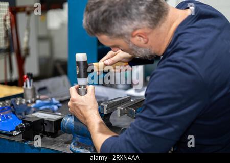 Professioneller Arbeiter, der in einer Metallwerkstatt an einem Stahlstück mit Hammer arbeitet. Industrielle Mechanik und Reparatur. Stockfoto