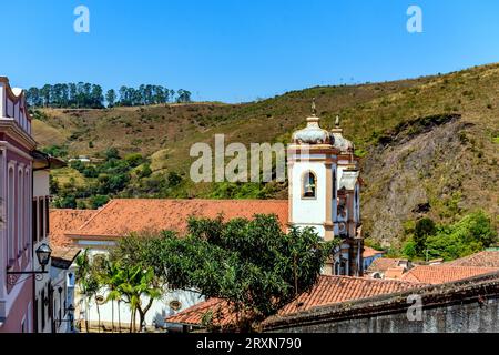 Turm der historischen Barockkirche zwischen den Häusern, Dächern und Hügeln in der Stadt Ouro Preto in Minas Gerais Stockfoto